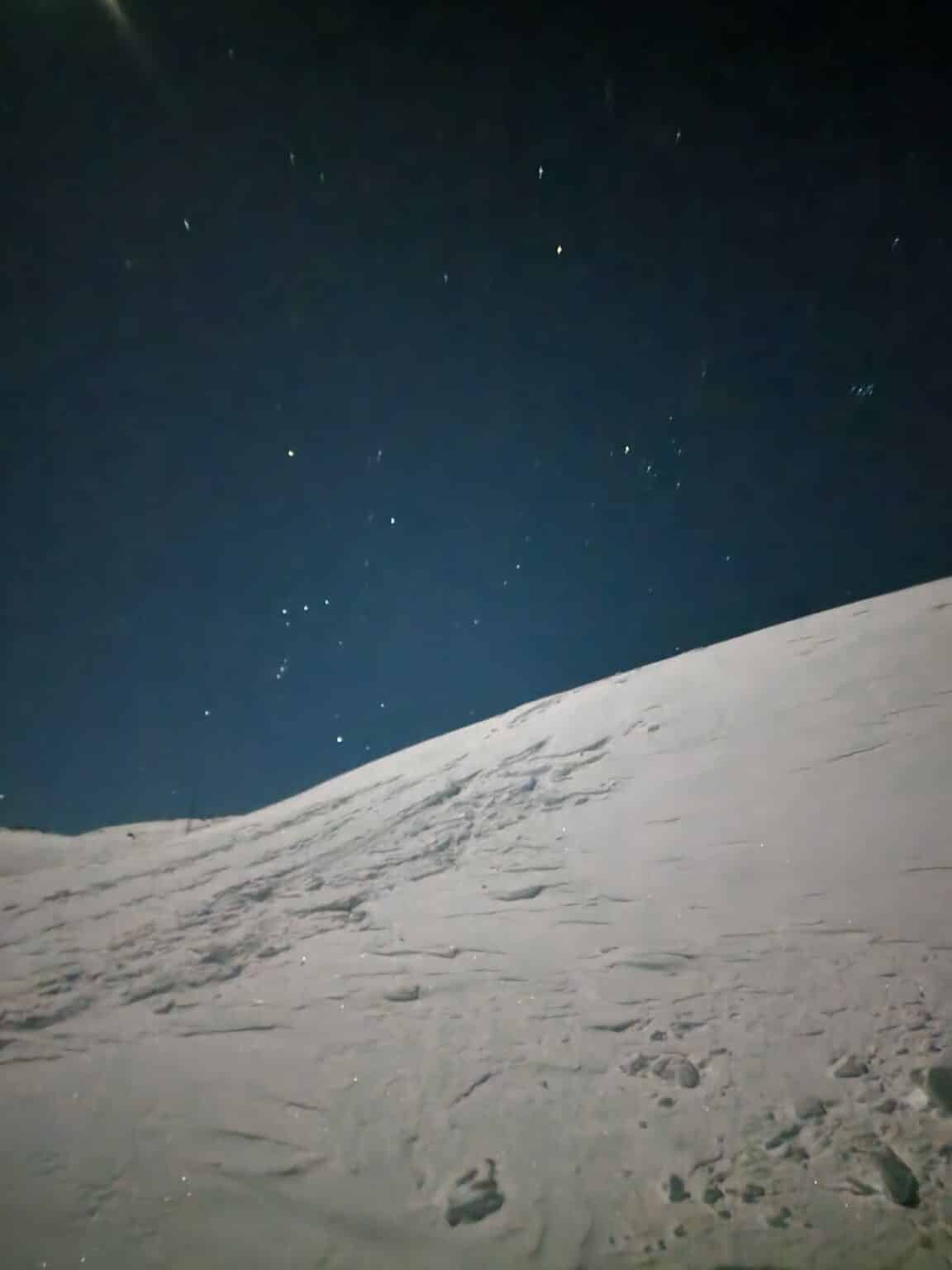En snødekt skråning under en klar nattehimmel med synlige stjerner.